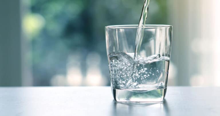 Pouring Fresh Drinking Water To A Glass On White Table