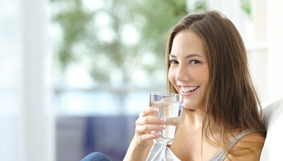 Smiling Woman Holding a Glass of Water — Spring Water Online in Mackay, QLD Smiling Woman Holding a Glass of Water — Spring Water Online in Mackay, QLD
