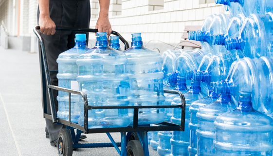 Delivery Man Pushing Trolley With Empty Water Bottles — Spring Water Online in Gladstone, QLD